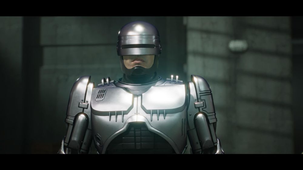 A screenshot from the video game: RoboCop: Rogue City - Unfinished Business. It shows the game's protagonist, RoboCop standing in front of and looking directly at the camera/screen. 