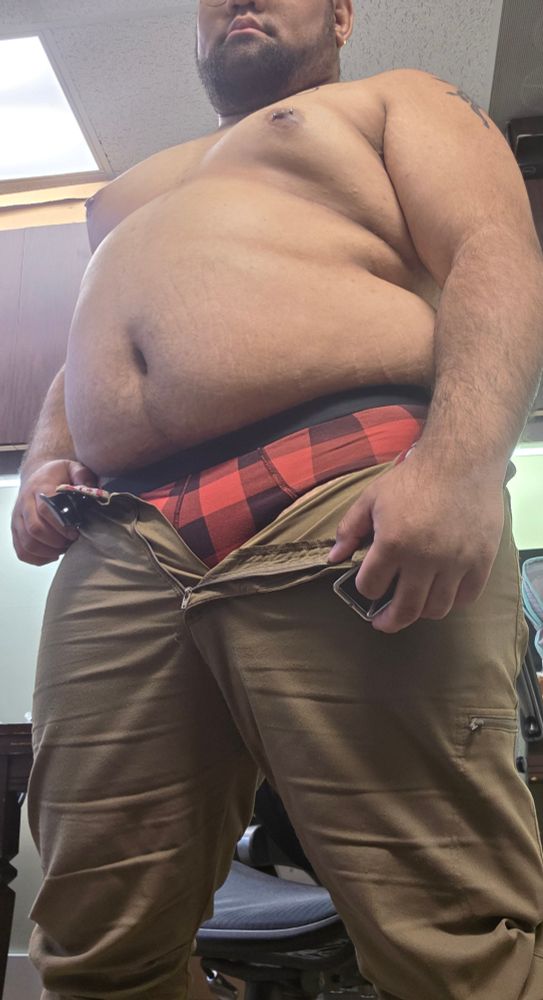I'm wearing a pair of khaki slacks with the zipper and button undone and a belt hanging open. A pair of red and black plaid briefs are peeking out. My belly is sticking out, and my pierced nipples emphasizing the curves of mt body. 