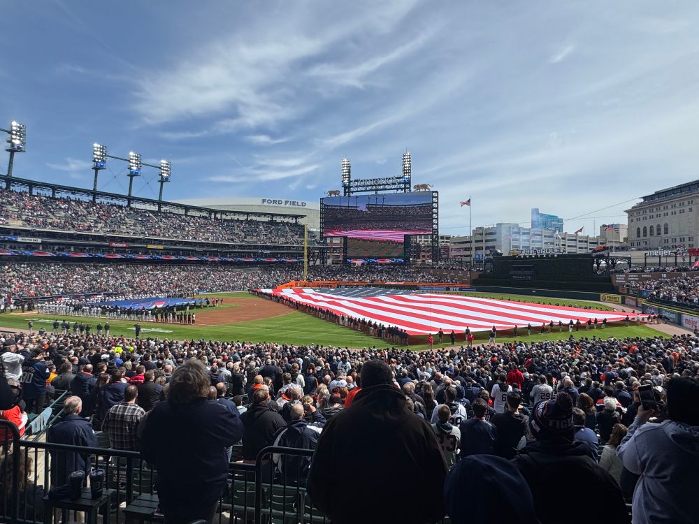 A large American flag in the outfield of a packed baseball stadium 