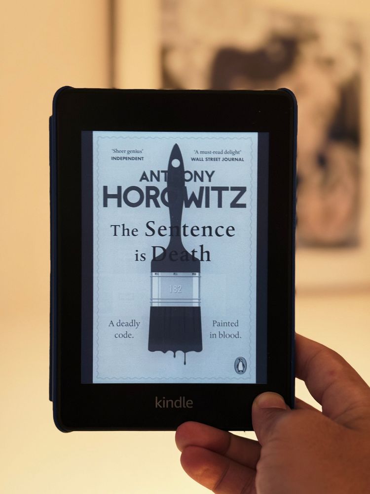 Een hand houdt een Kindle vast waarop het boek The Sentence is Death van Anthony Horowitz wordt getoond.