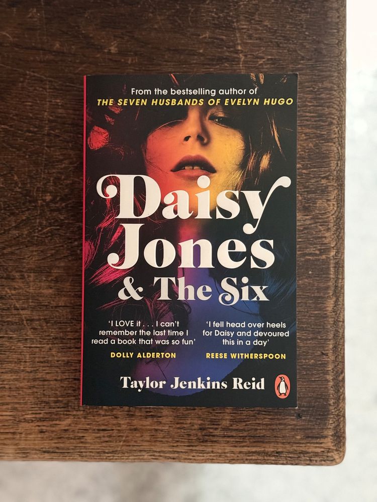 Een boek met de titel Daisy Jones & The Six van Taylor Jenkins Reid ligt op een houten oppervlak.