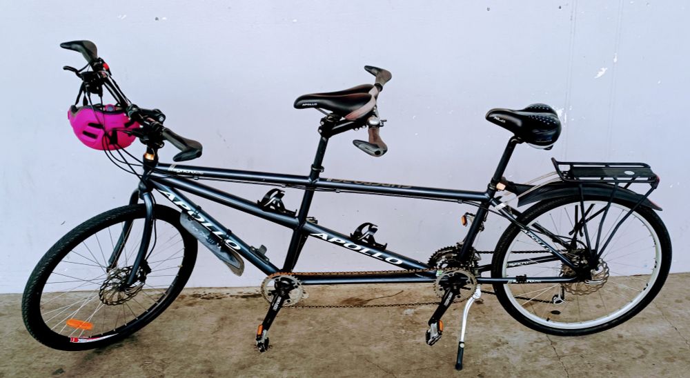 A photo of a tandem bicycle in front of a great wall. A purple helmet hangs from the front handlebars.