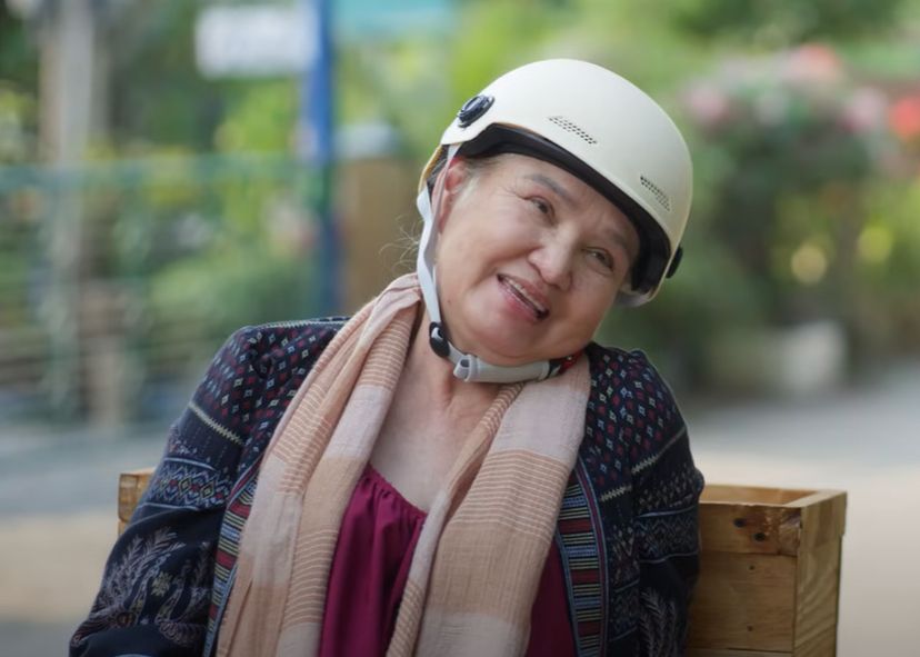 Screenshot of the thai serie My Sweatheart Jom, Episode 7.

We see the granny, with her helmet on the head, still on her quad, smiling at Yo and Jom, out of the frame.
Jom asked Yo to feel his arm and asked him  if it was hard. Yo asked back what was hard, with a choked look. Jom asked again if his arm muscle was hard, so to tell Yo he was strong. 
All this conversation, not very subtle, made that smile on granny's face, she seems to say "aaah young lovers..."