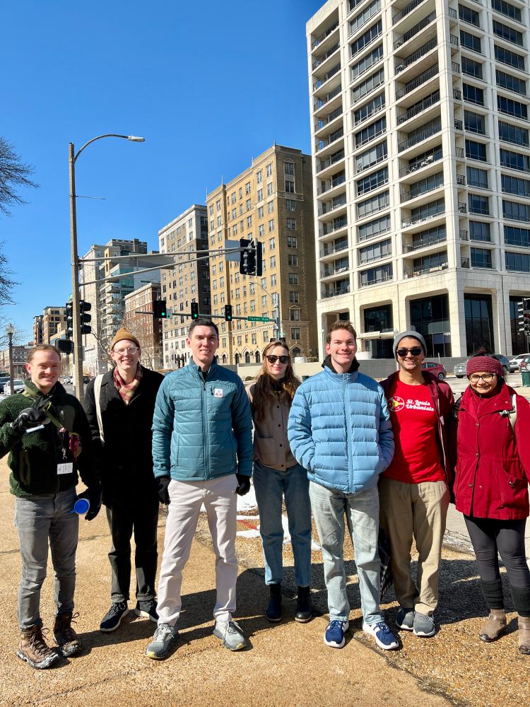  a small group of young urbanists take a picture together on Lindell Boulevard. Several mid-rise buildings can be seen behind them. 