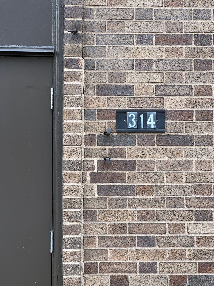 A close shot of one of the doors. It is dark brown, made of metal. Next to it, on the brown brick, three numbers show the address: 314. It happens to also be the area code for most St. Louis area phone numbers. 