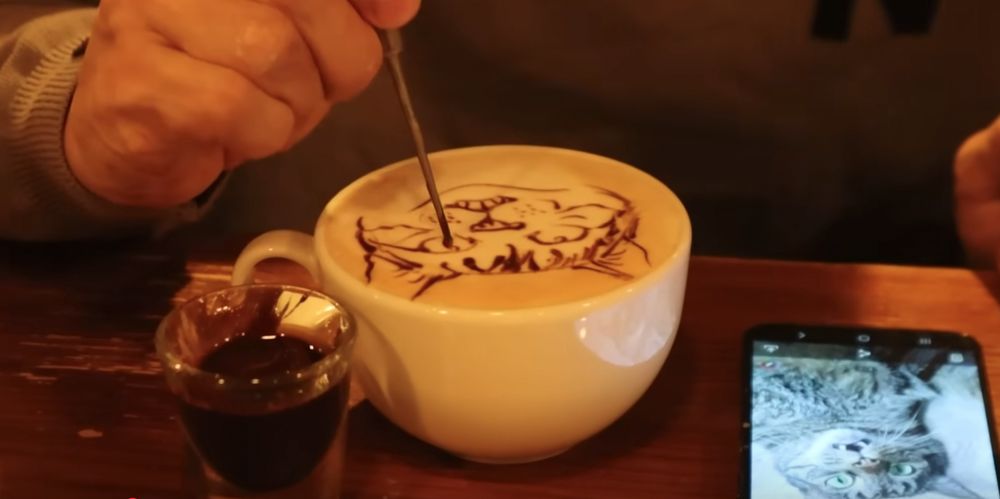 an employee in a Tokyo coffee shop drawing a cat's face on latte foam using chocolate