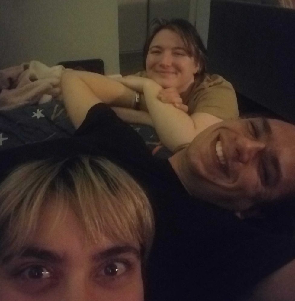 Three happy faces smile in a close-up, selfie-style photo, snuggled up on a couch together. The quality is grainy and the lighting dim - clearly this photo was taken at night. Nevertheless, the light of gleeful triumph gleams in the eyes of the person at the bottom of the photo.