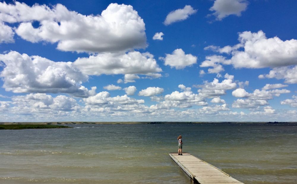 Me, standing on the end of a dock projecting out into a prairie lake with big blue sky full of puffy white clouds overhead.