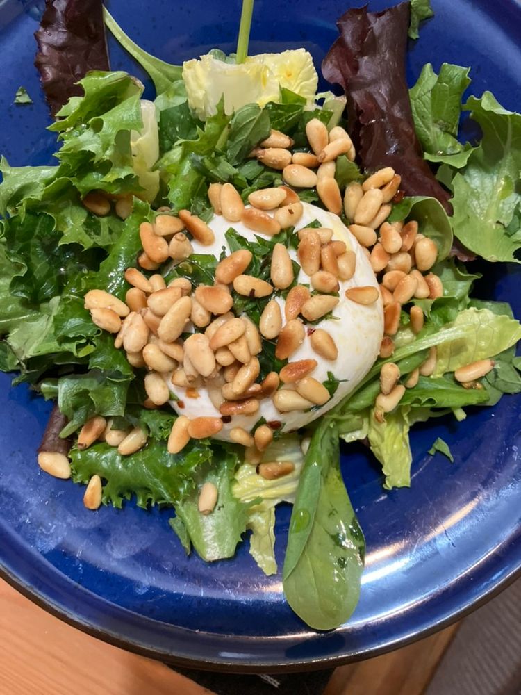 Image of a salad with greens, pine nuts, and burrata in a blue bowl.