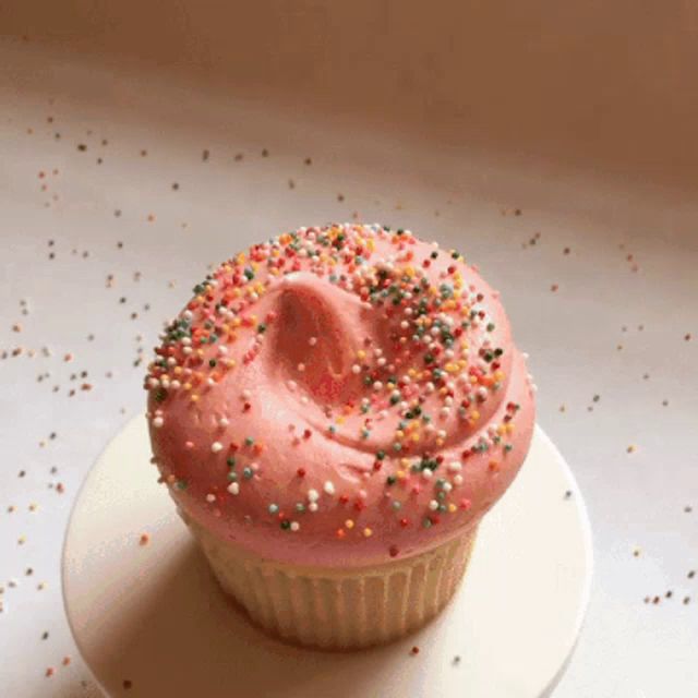 a cupcake with pink frosting and colorful sprinkles