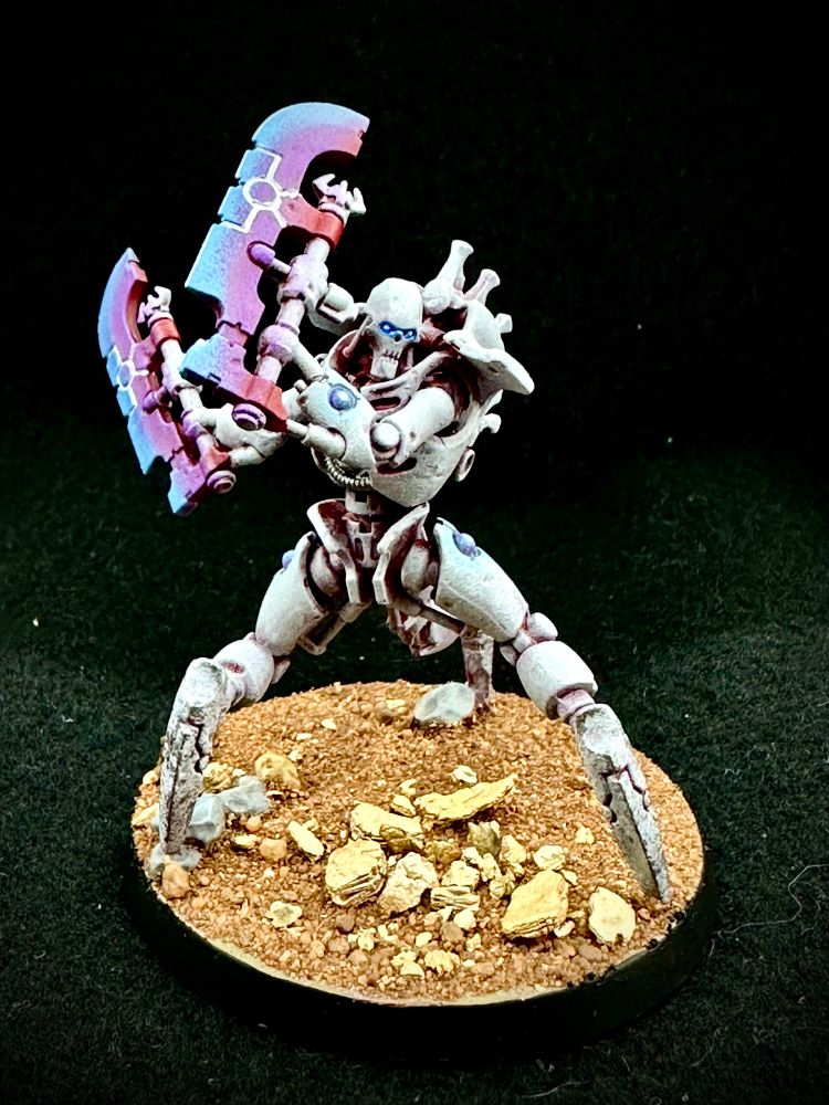 A necron skorphek destroyer in white with blue/purple power blade stands on a desert base
