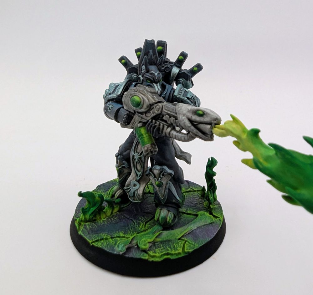 Blue-grey chaos space marine wielding a warp flamethrower shooting out a stream of green flame. They stand on a cracked purple surface with green flames erupting from the cracks.