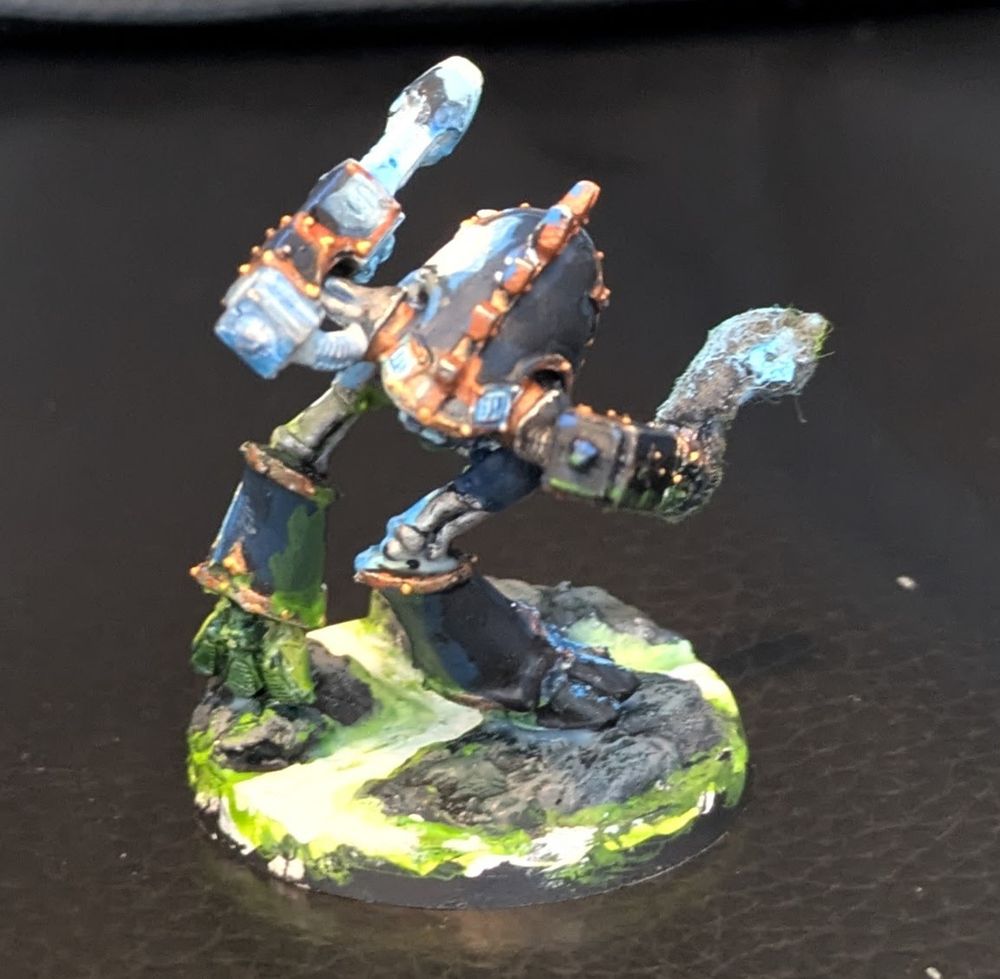 Various angles of an old Epic Warhound Titan standing on a rocky field with glowing green stuff flowing through the broken earth. It's right arm is a lowered gatling mega bolter with smoke pouring out, while it's left arm is a raised plasma blaster in firing position, spreading a blue glow over the left side of the Warhound. The green stuff flowing under it casts a green light on the underside of the Titan. The colors of the titan that are not lit up are a muted dark blue with copper trim