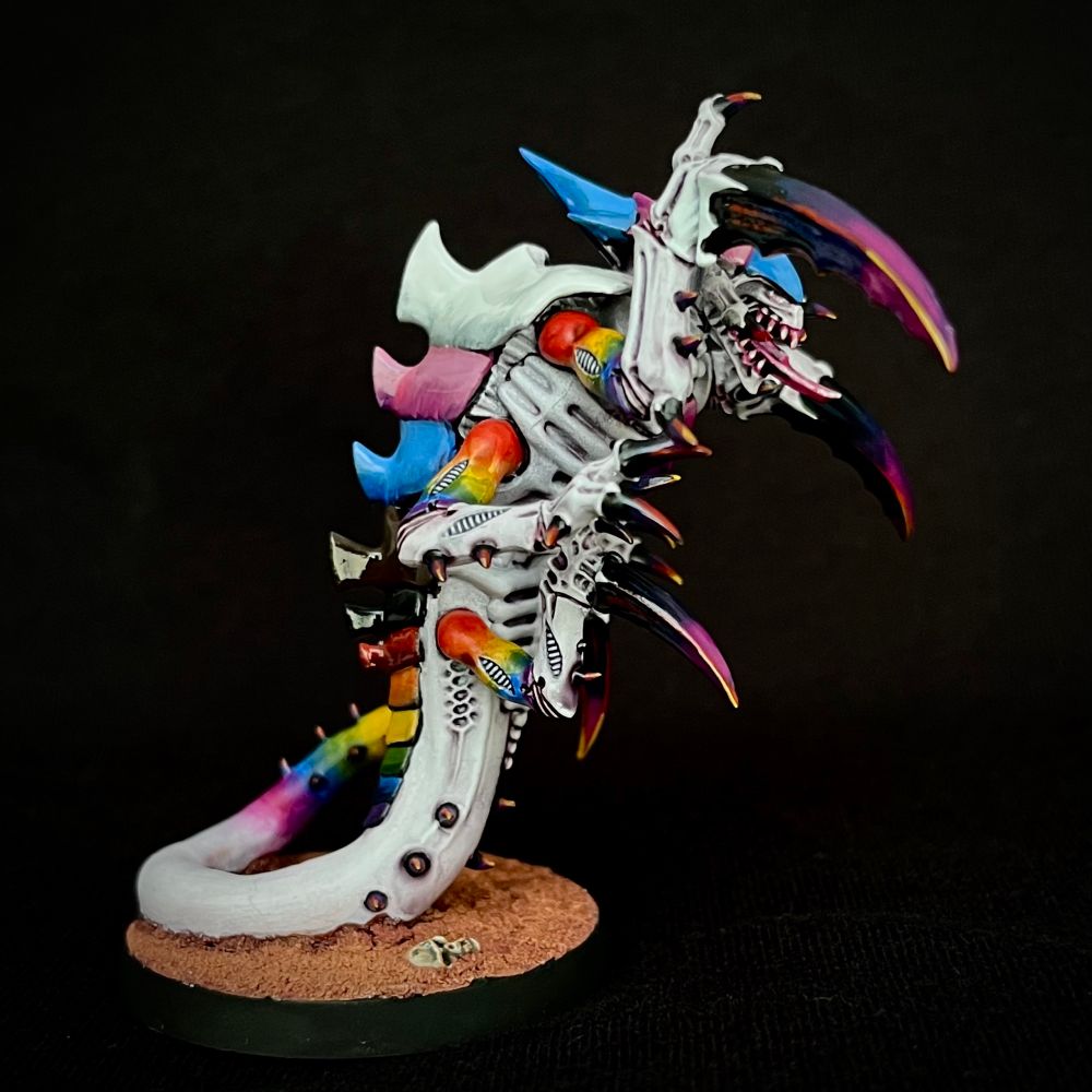 A Tyranid Ravener painted with whiteish purplish skin. Its upper arms and tail end are rainbow-hued, and its claws are purple.
It’s carapace plates are each painted a solid colour: the head matches the trans pride flag, the chest matches the bisexual pride flag, the tail matches the non-binary flag and the back matches the progress pride flag.
This Tyranid eats fascists.
