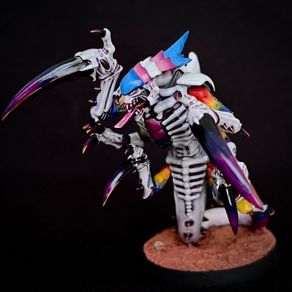 A Tyranid Ravener painted with whiteish purplish skin. Its upper arms and tail end are rainbow-hued, and its claws are purple.
It’s carapace plates are each painted a solid colour: the head matches the trans pride flag, the chest matches the bisexual pride flag, the tail matches the non-binary flag and the back matches the progress pride flag.
This Tyranid eats fascists.