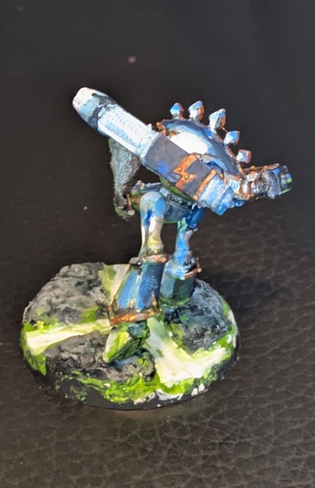 Various angles of an old Epic Warhound Titan standing on a rocky field with glowing green stuff flowing through the broken earth. It's right arm is a lowered gatling mega bolter with smoke pouring out, while it's left arm is a raised plasma blaster in firing position, spreading a blue glow over the left side of the Warhound. The green stuff flowing under it casts a green light on the underside of the Titan. The colors of the titan that are not lit up are a muted dark blue with copper trim