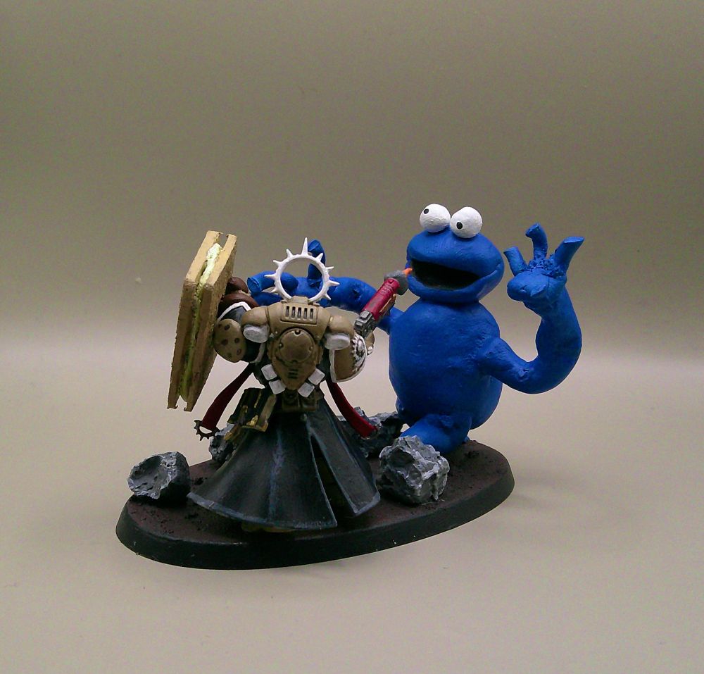 A chaplain miniature with an assault trooper head and his crozius replaced with an MDF / green stuff shield in the design of a custard cream. He is shooting at the Cookie Monster who is also made of green stuff.