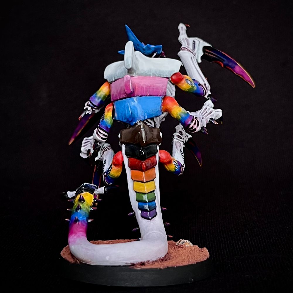 A Tyranid Ravener painted with whiteish purplish skin. Its upper arms and tail end are rainbow-hued, and its claws are purple.
It’s carapace plates are each painted a solid colour: the head matches the trans pride flag, the chest matches the bisexual pride flag, the tail matches the non-binary flag and the back matches the progress pride flag.
This Tyranid eats fascists.