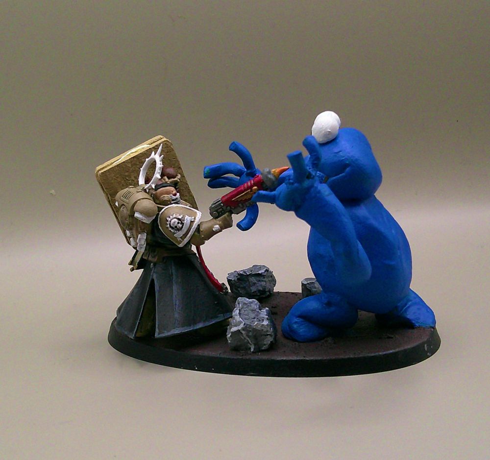 A chaplain miniature with an assault trooper head and his crozius replaced with an MDF / green stuff shield in the design of a custard cream. He is shooting at the Cookie Monster who is also made of green stuff.