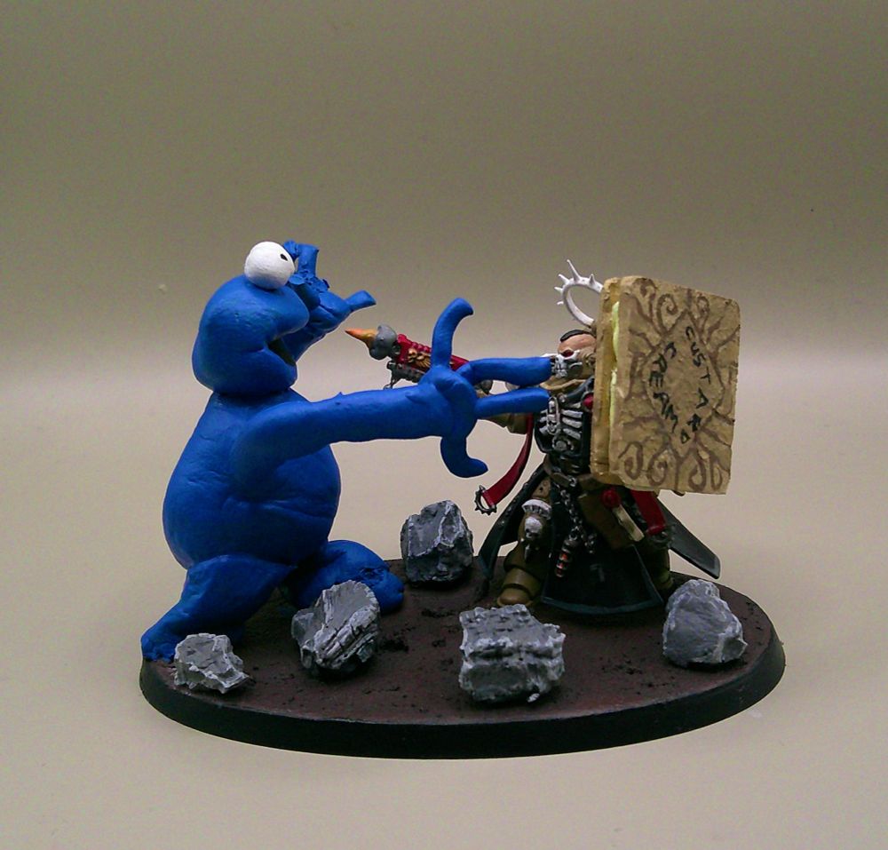 A chaplain miniature with an assault trooper head and his crozius replaced with an MDF / green stuff shield in the design of a custard cream. He is shooting at the Cookie Monster who is also made of green stuff.