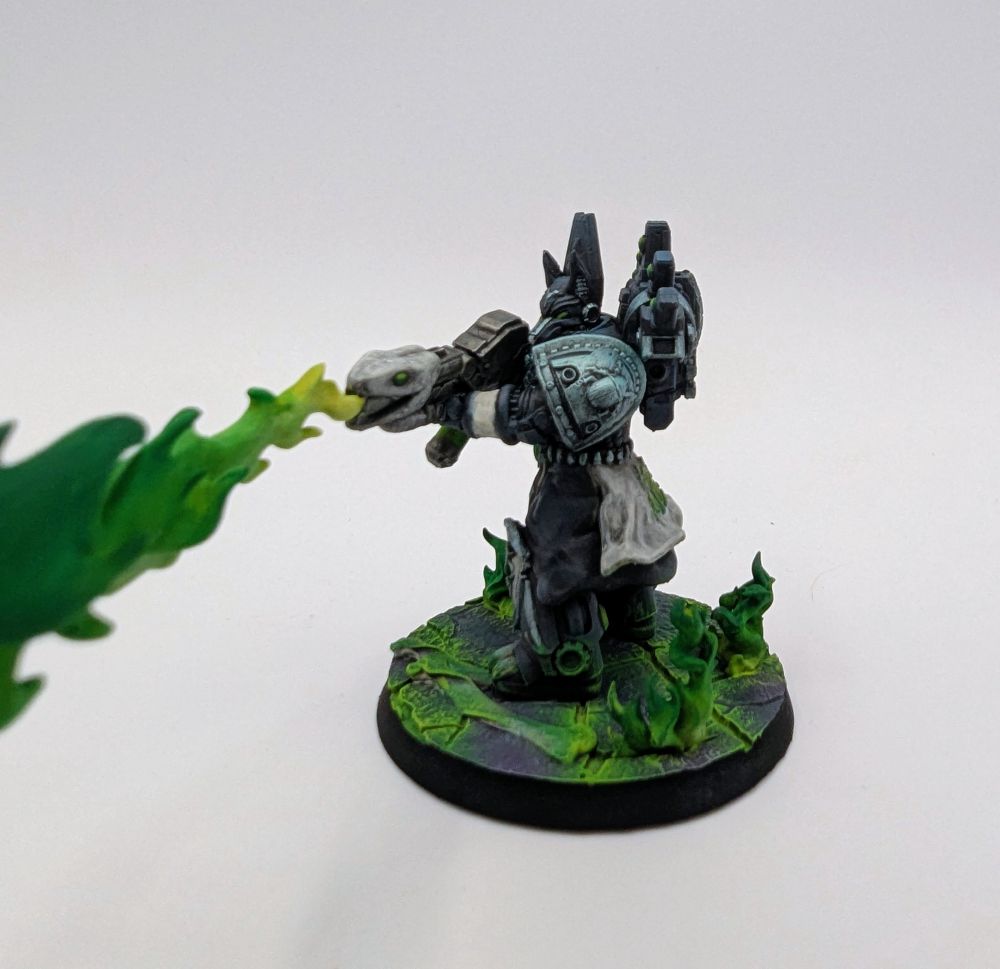 Blue-grey chaos space marine wielding a warp flamethrower shooting out a stream of green flame. They stand on a cracked purple surface with green flames erupting from the cracks.