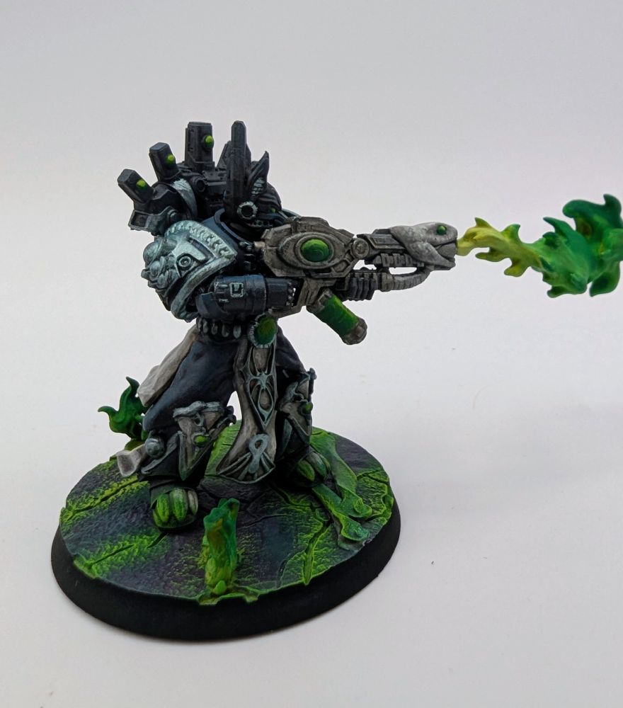 Blue-grey chaos space marine wielding a warp flamethrower shooting out a stream of green flame. They stand on a cracked purple surface with green flames erupting from the cracks.