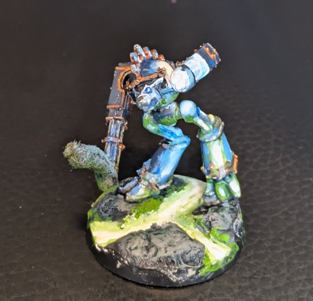 Various angles of an old Epic Warhound Titan standing on a rocky field with glowing green stuff flowing through the broken earth. It's right arm is a lowered gatling mega bolter with smoke pouring out, while it's left arm is a raised plasma blaster in firing position, spreading a blue glow over the left side of the Warhound. The green stuff flowing under it casts a green light on the underside of the Titan. The colors of the titan that are not lit up are a muted dark blue with copper trim
