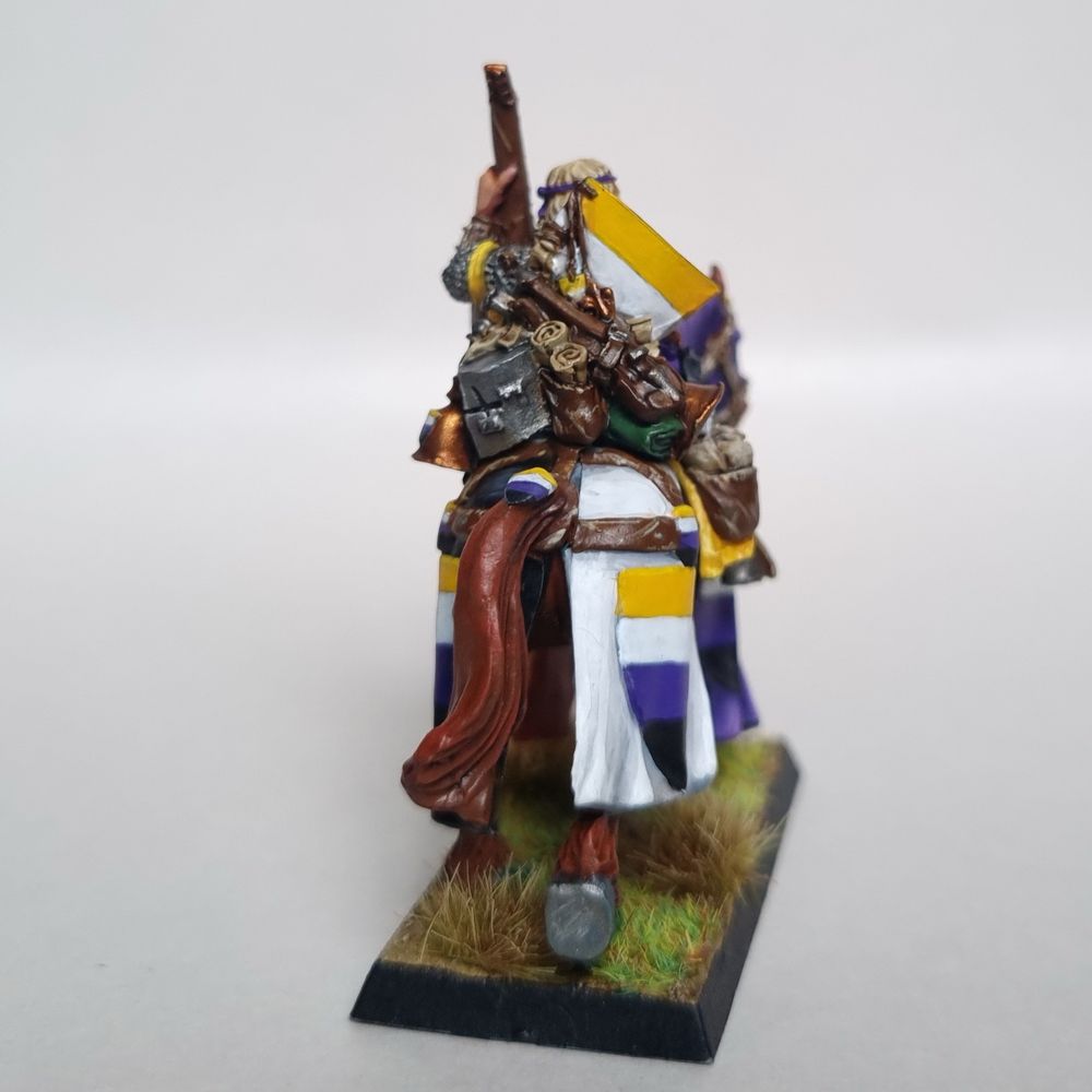 A Bretonnian questing knight musician. They wear the coat of arms and colour scheme of the non-binary flag.