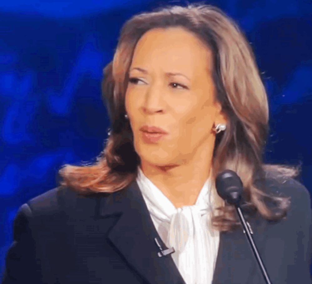 a woman in a suit is speaking into a microphone and making a funny face