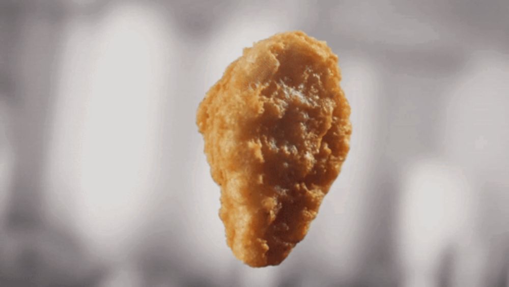 a fried chicken nugget with a bite taken out of it is floating in the air