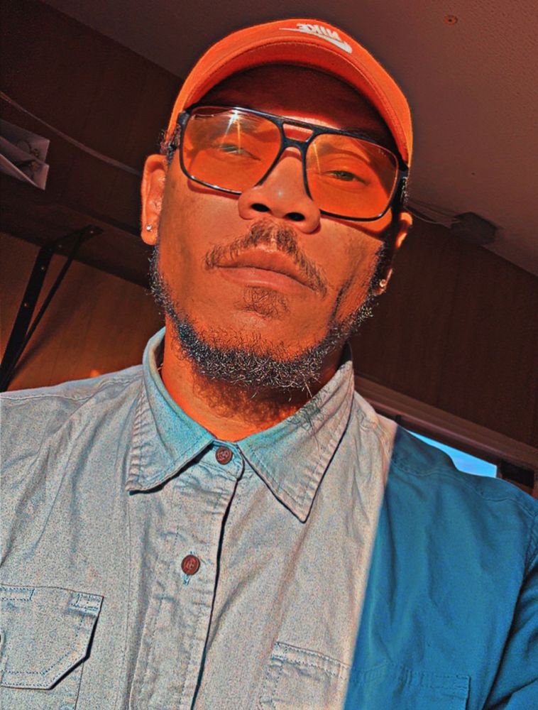 A man wearing an orange hat and orange tinted sunglasses with a teal shirt