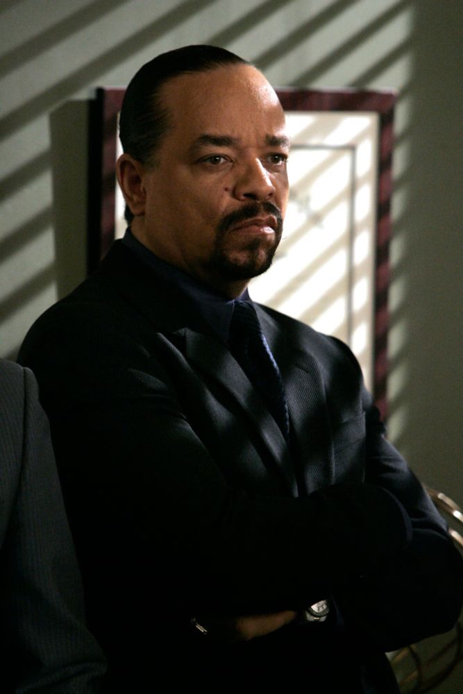 Ice-T stands in an office with his arms folded while the sunlight filters through the blinds 