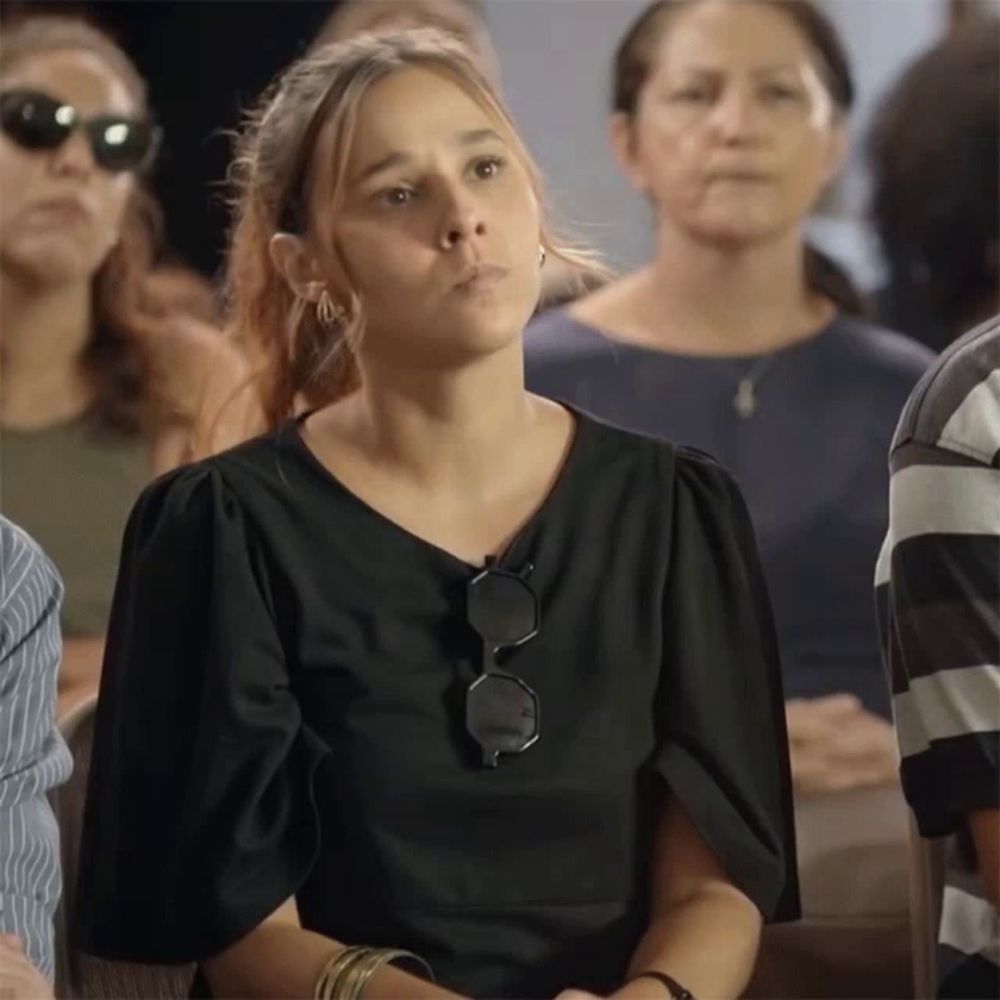 a woman wearing sunglasses and a black shirt sits in a crowd of people