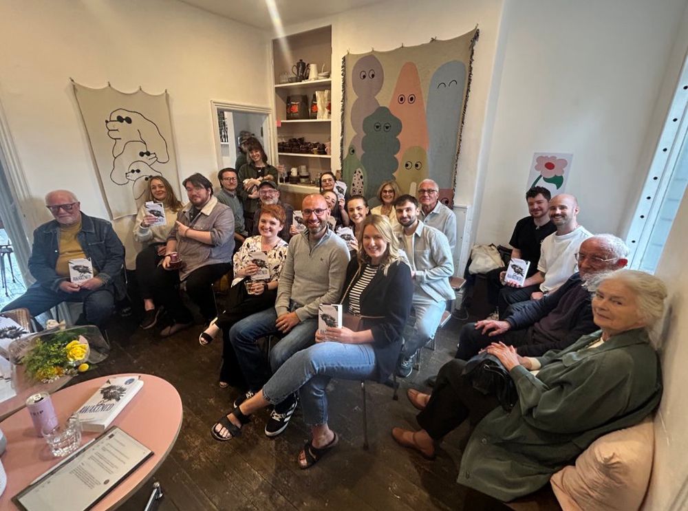 A large group of people sitting in a bookshop holding copies of Awakened and smiling at the camera