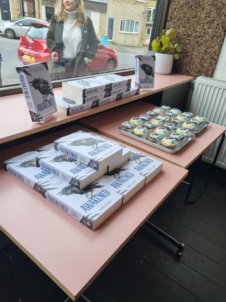 A table in a bookshop laid out with copies of the book Awakened, alongside a tray of cupcakes with the book  cover on them