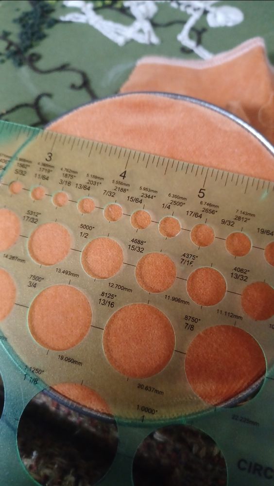 A green circle template on top of orange velvet in an antique metal embroidery hoop. 