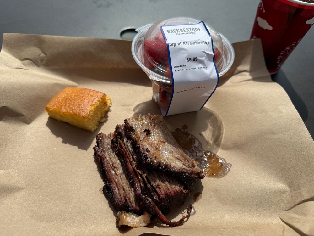 A platter with brisket, cornbread, and a fruit cup. 
