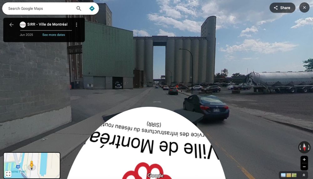Google Streetview of Rue Mill in Montreal, looking west towards the Farine Five Roses plant. The street is flanked by a number of industrial buildings, silos, and a parking lot with a delivery truck in it. No people are seen in the photo. 