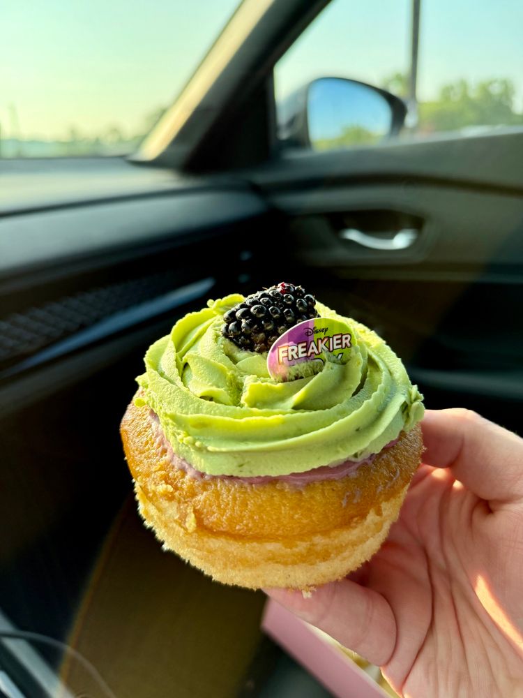 A photo of me holding the Freakier Friday cake from Crumbl. It has a green frosting with blackberry glaze with a blackberry on top.