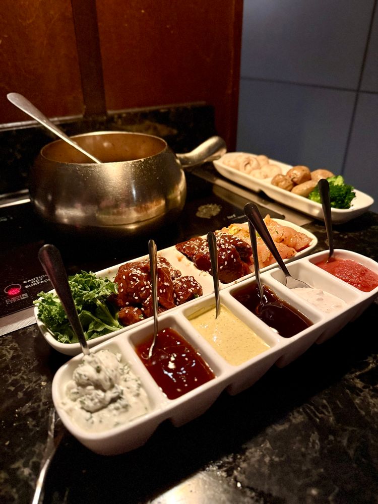 Coq Au Vin fondue with various sauces, vegetables, chicken and steak.