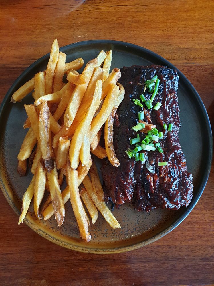 BBQ ribs with brown glaze and green onion sprinkles on the right and golden potato fries of the left of the picture. 