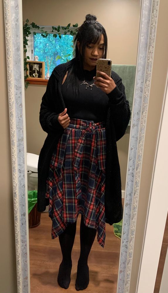 Pic of me, wearing a knee length tartan skirt, black mock turtleneck tank top, nordic rune necklace and long black cardigan
