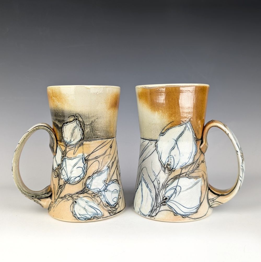 Two tall handmade mugs illustrated with leaves. 