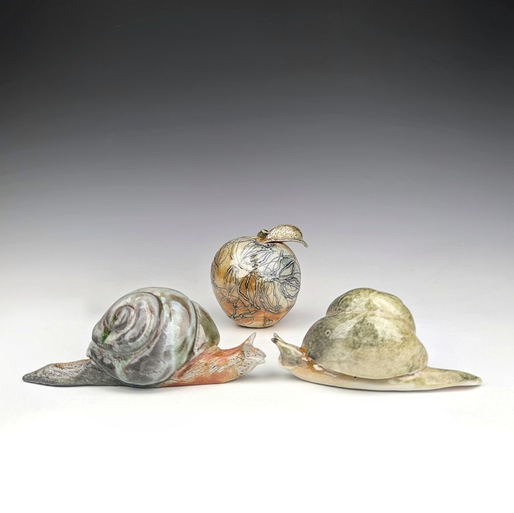 Two ceramic snails facing each other with a ceramic apple in behind them.