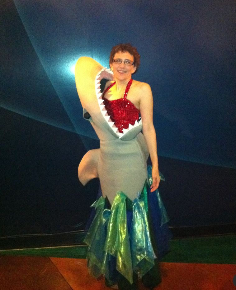 A costume depicting the wearer, in sparkly swimsuit, protruding from the mouth of a shark. Hem evokes water. 
