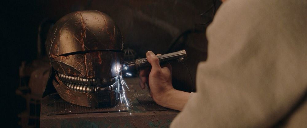 The Stranger from The Acolyte working on refining his helmet. His helmet is on a table and he’s welding cracks in the helmet.