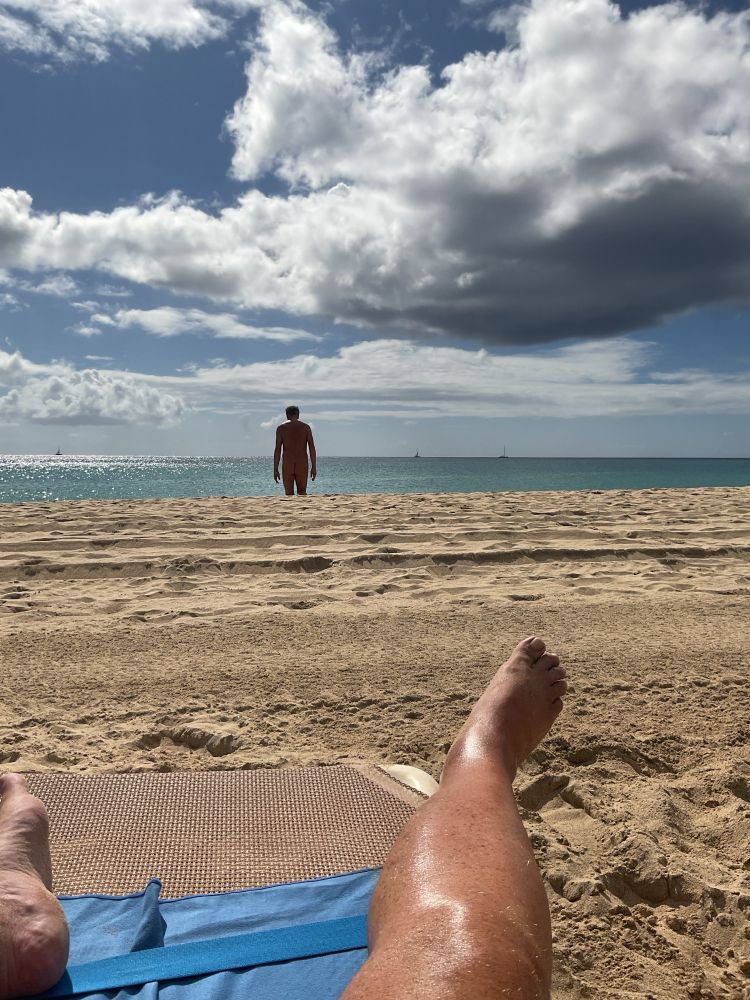 Leg and sun lounger on a sandy beach and someone walking towards the sea