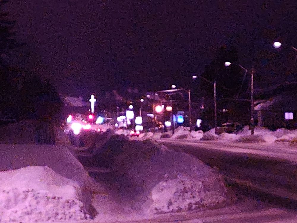 A blurry zoomed photo, with what seems to be a reddish pink film grain, of a city road, with a massive luminous cross in the distance. It seethes