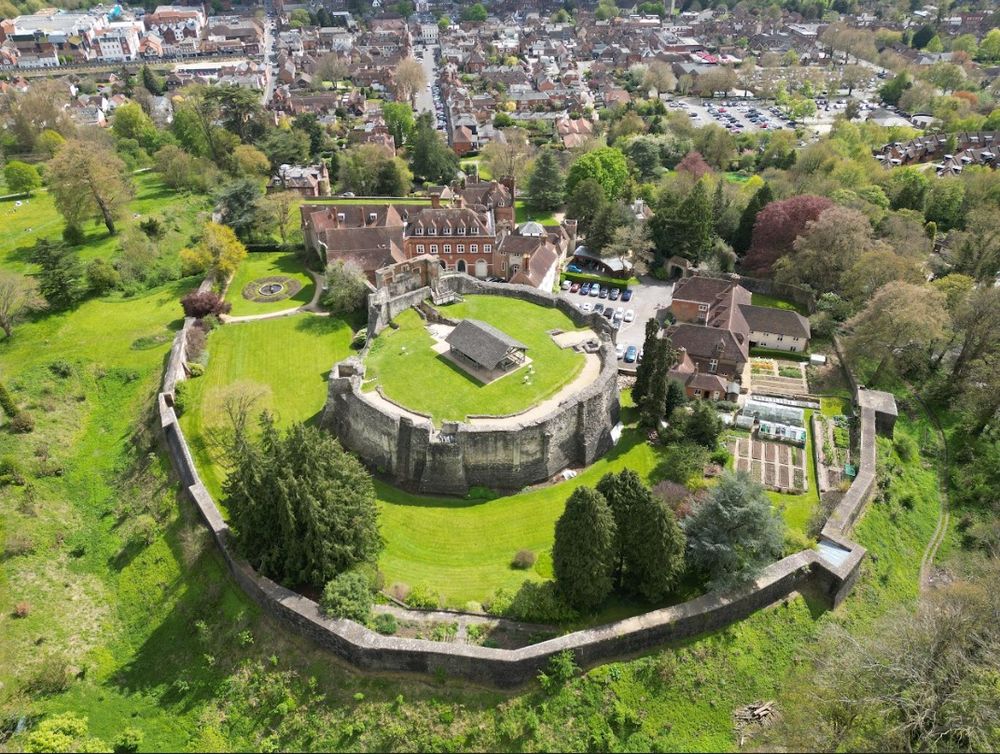 An aerial view of Farnham Castle in Surrey, England. The castle stands majestically on a hilltop, showcasing its medieval architecture, stone walls, and lush green grounds.