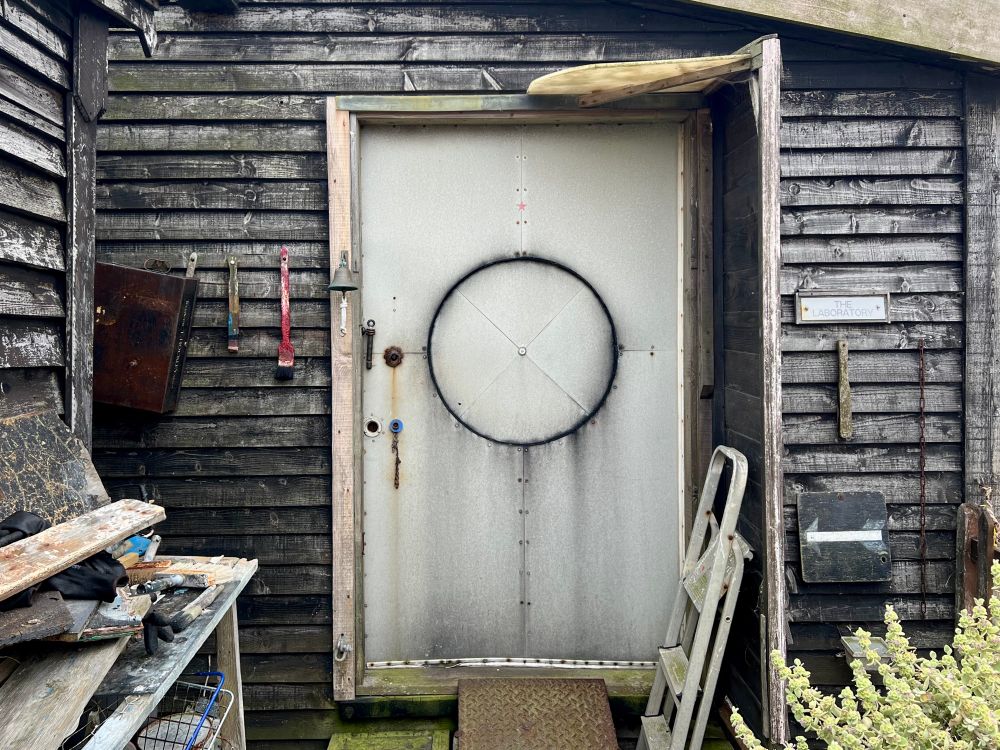 Black timber shed with galvanised metal door that has a black painted circle inscribed into it